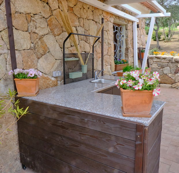 Blumen in Terracottapflanzgefässen auf der Ablage einer Aussenküche an einem Ferienhaus.